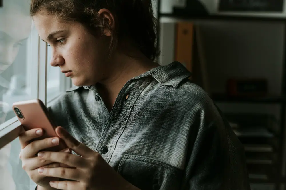 Mulher olhando o celular em silêncio, refletindo sobre sua vida ao ver rotinas perfeitas no Instagram